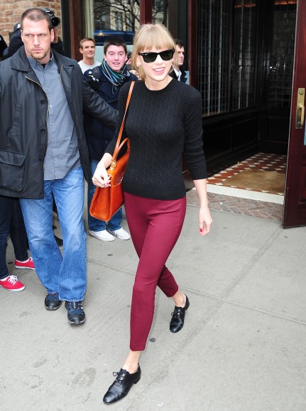Taylor Swift wearing a black cable knit sweater and cropped red pants
